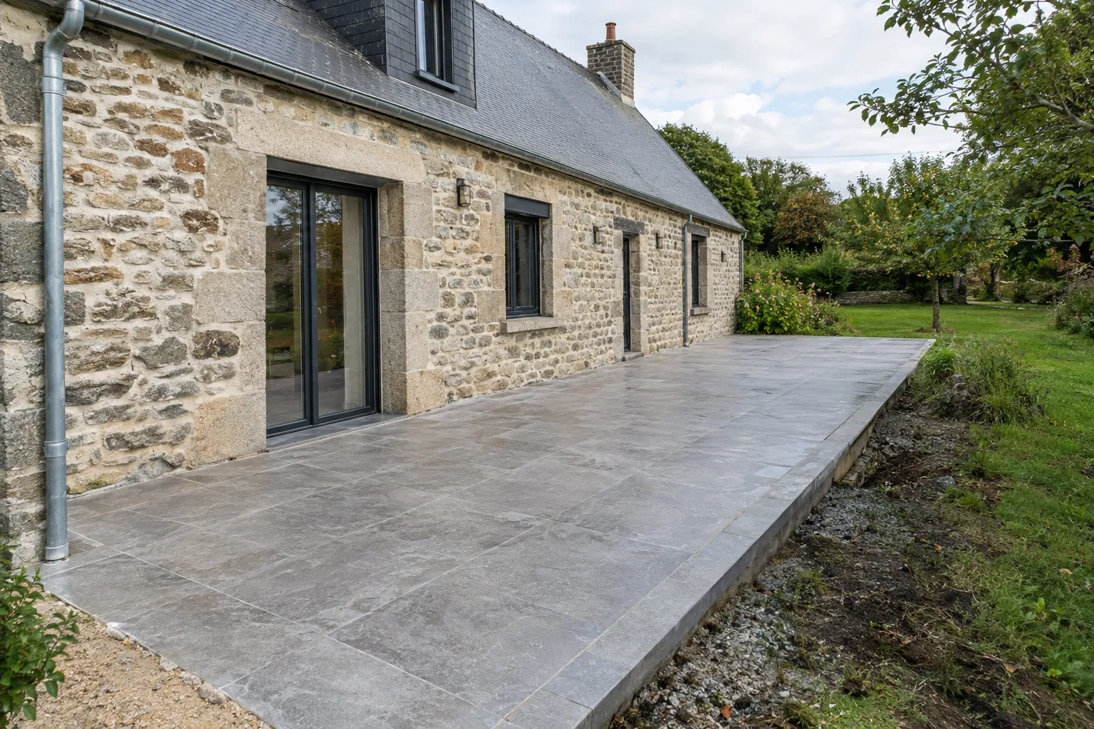 Terrasse carrelée en grès aspect pierre à Châteaumeillant, devant une maison de bourg et son jardin